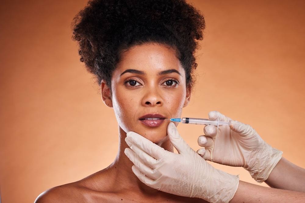 Woman receiving a lip filler injection, representing aesthetic enhancement and the choice between Sculptra and dermal fillers for facial augmentation.